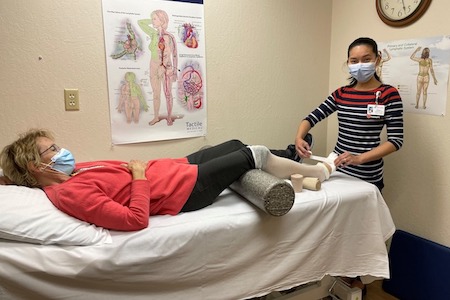 Tifanee Lin, OTR/L, CLT-LANA, wraps a patient's leg during a therapy session.